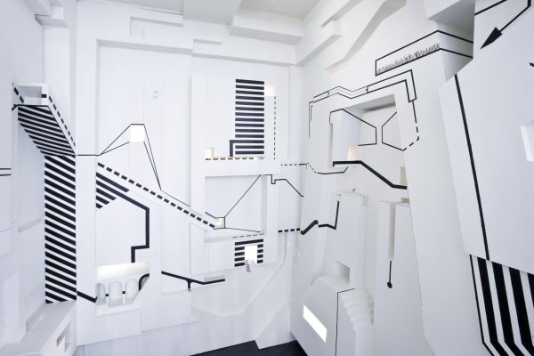 Black lines, resembling graph markers or map keys, appear on the walls of an ornate, small white space