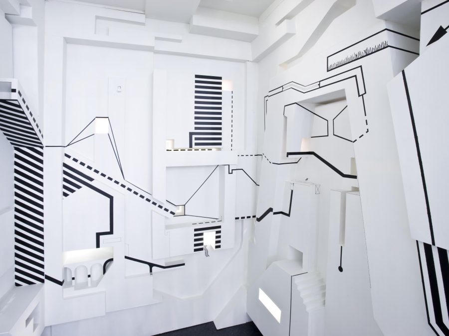 Black lines, resembling graph markers or map keys, appear on the walls of an ornate, small white space