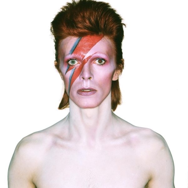 A shirtless David Bowie with a painted red lighting bolt with blue accent from his forehead down through his right eye and cheek