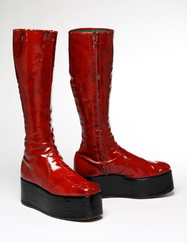 Red, chunky, high-top platform boots stand erect in a white room.