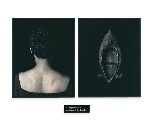 Two framed black and white pictures. The one on the left features a portrait with the person's back turned toward the viewer; the right image is of the back of a wooden mask. A small plaque appears under the frames.
