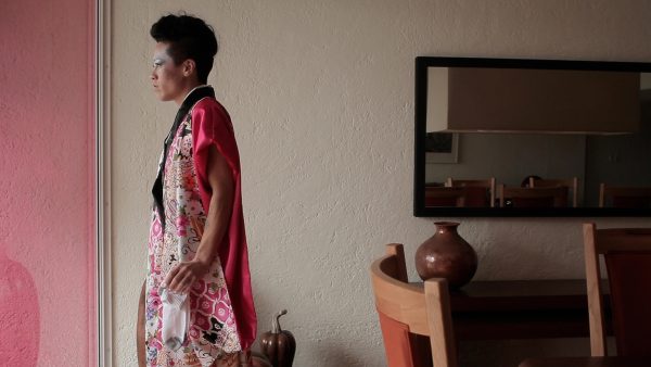A person stares off to the viewer's left in a hotel room.