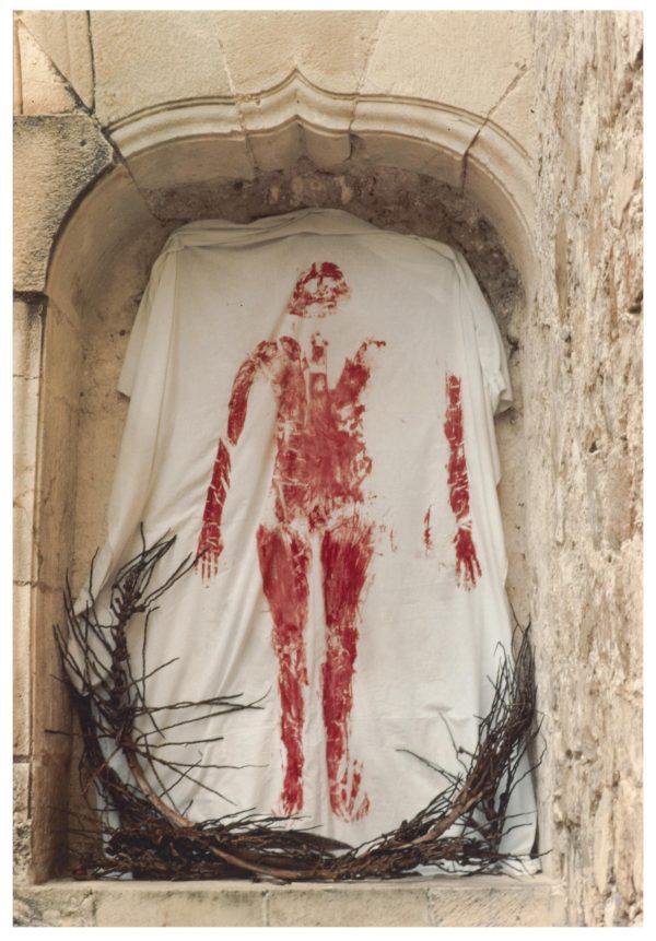 A white sheet with a blood-red imprint of a body hangs in a stone niche.
