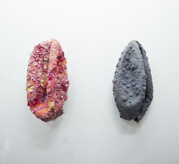 Two deflated balls, one pink, one grey, on a white wall.