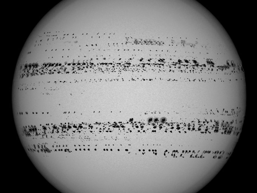 A grey orb against a black background with hundreds of black dots that form lines in the upper- and lower-middle portions