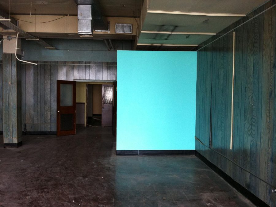 A blue wall glows in a dark gallery space