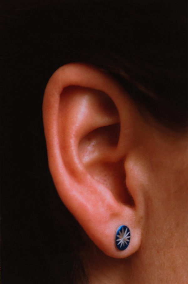 A close-up photograph shows a light-skinned person's ear wearing a blue earring with a star on it.