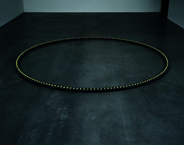A dark circle with tiny lights all around it lays flat on the floor in a dark room