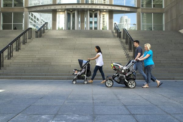 Three adults pushing strollers across the MCA Plaza on a sunny day