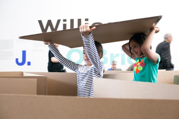 Two children carrying a cardboard sheet through a cardboard maze