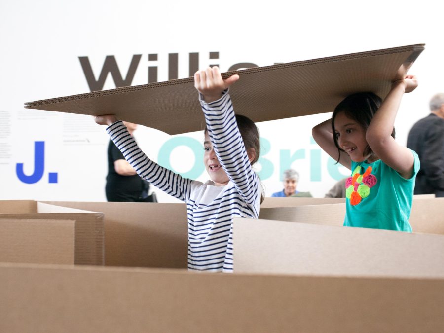 Two children carrying a cardboard sheet through a cardboard maze