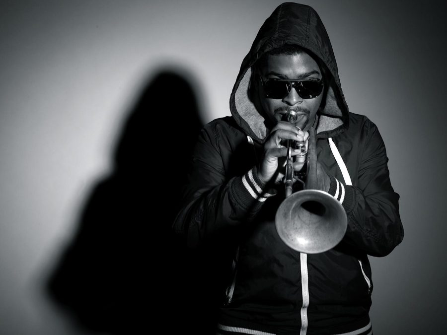 Black and white portrait of a male presenting person in a hoodie blowing into a trumpet
