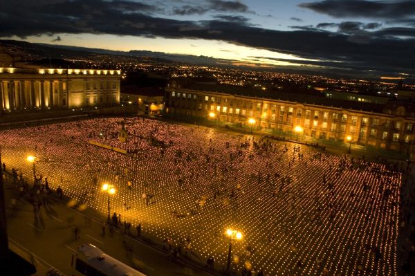 A large plaza at dusk filled with people in and around rows and rows of candles