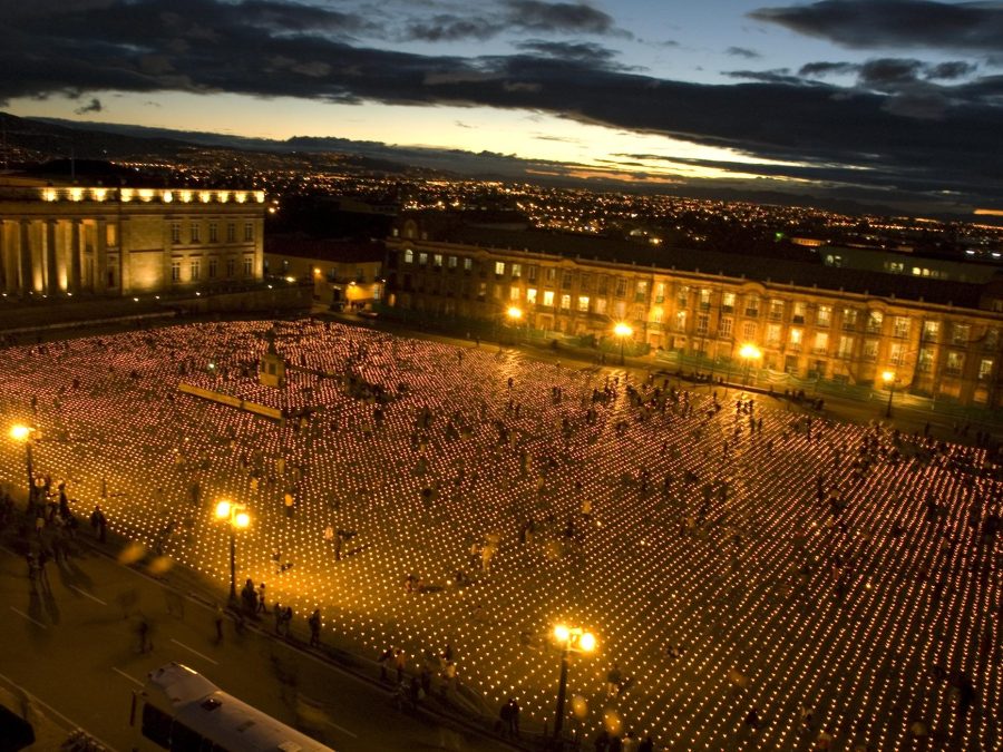 A large plaza at dusk filled with people in and around rows and rows of candles