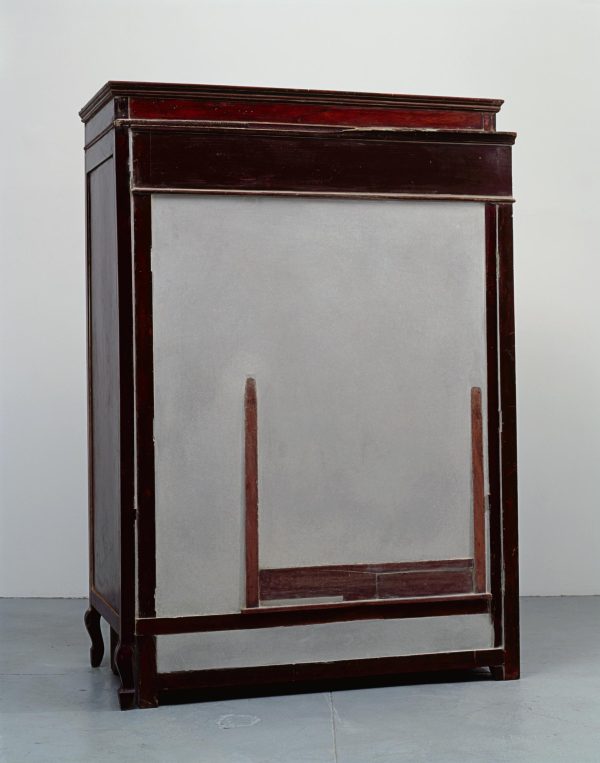 A wooden cabinet filed with cement has a barely visible second piece of furniture peeking out the surface.