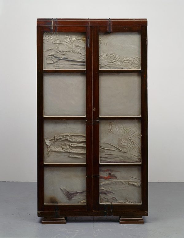 A sculpture of a wooden chest is filled with cement that has creases and ripples on the surface.