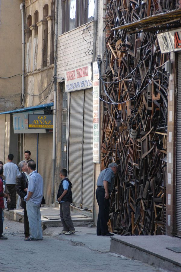 Several passerby look at a massive pile of hundreds of chairs placed between two tall buildings.