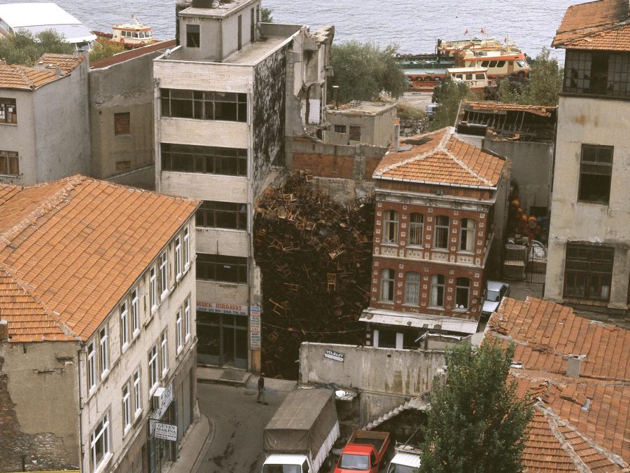 Overhead view of old buildings near a body of water. Between two buildings is a pile of chairs three stories high.