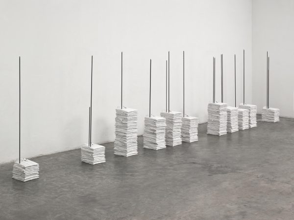 A sculpture shows several stacks of folded white polo shirts that are pierced by metal rods sticking out of the floor.