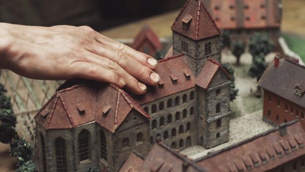 A light-skinned right hand touches the roof of a small scale model of a castle complex
