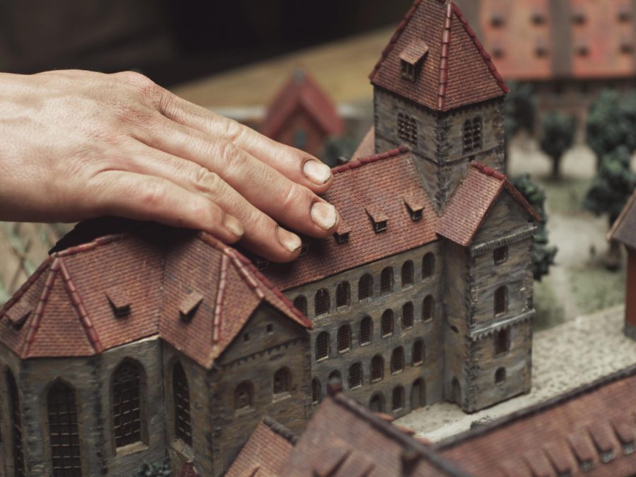 A light-skinned right hand touches the roof of a small scale model of a castle complex