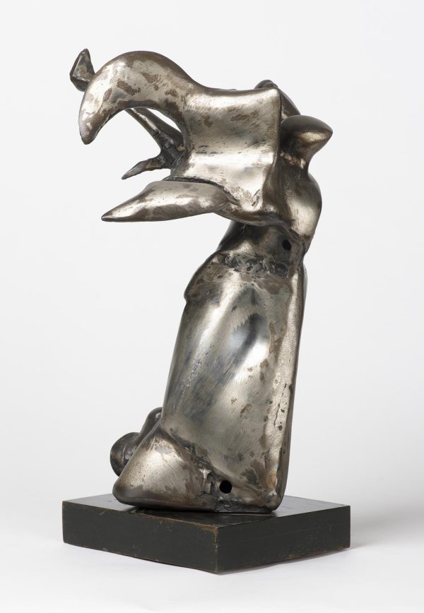 A silver sculpture on a short black pedestal. The top half has several talon like forms coming out of it while the bottom half is more stagnant