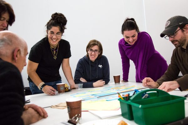 A group of adults gather around a table with disposable coffee mugs and art-making supplies