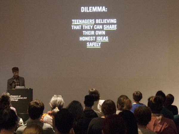 A group of people look up at a presentation slide with just white text against a black background reading Dilemma, teenagers believing that they can share their own honest ideas safely
