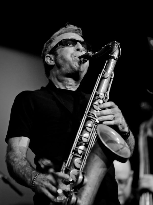 Black-and-white photograph of a man wearing sunglasses indoors playing a saxaphone