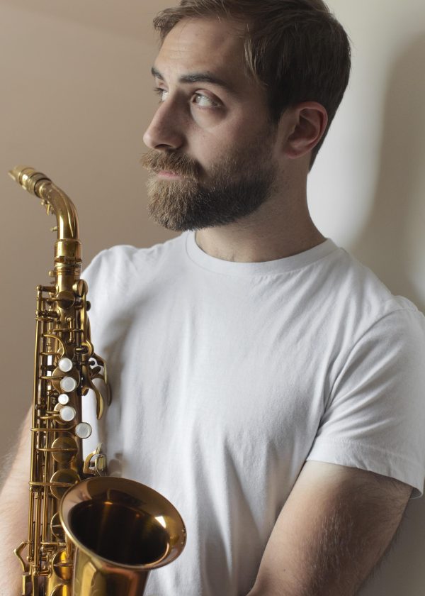 Portrait of a bearded young man holding a saxophone to his chest
