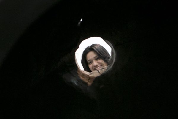 Pitch black environment pierced by a small hole, which leads to bright light and a woman's smiling face