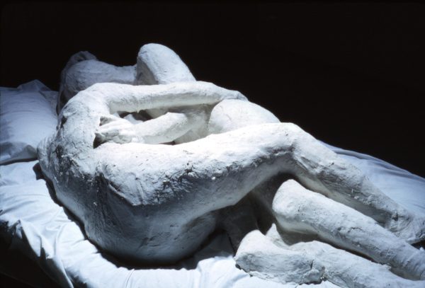 Dramatically lit image of two plaster figures entwined on a bed