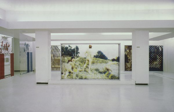 Large artworks hang between columns throughout a large basement-like space