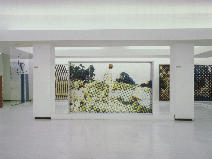 Large artworks hang between columns throughout a large basement-like space