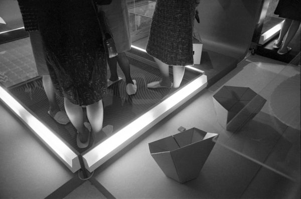 Black and white photo of a group of people standing in a small lit square area as viewed from their shoulders down