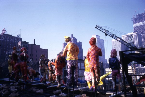 Giant human figures on a rooftop amid a city skyline and a crane