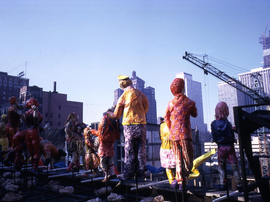 Giant human figures on a rooftop amid a city skyline and a crane