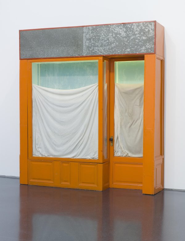 A door and a large window covered in white sheets surrounded by an orange frame next to a white wall