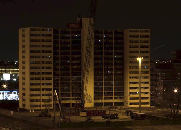An abandoned high rise building at night illuminated by the glow of one tall streetlight