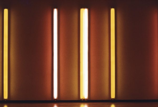 Four orange and yellow neon lights hung horizontally illuminate a wall
