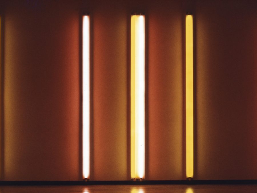 Four orange and yellow neon lights hung horizontally illuminate a wall