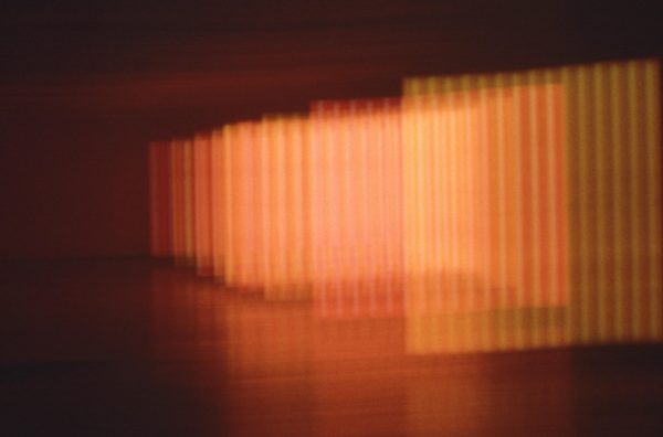 Blurry bars of neon form several orange squares in a room extending to the back of a darkened room