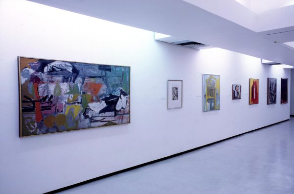 Many colorful paintings hang along a gallery wall.