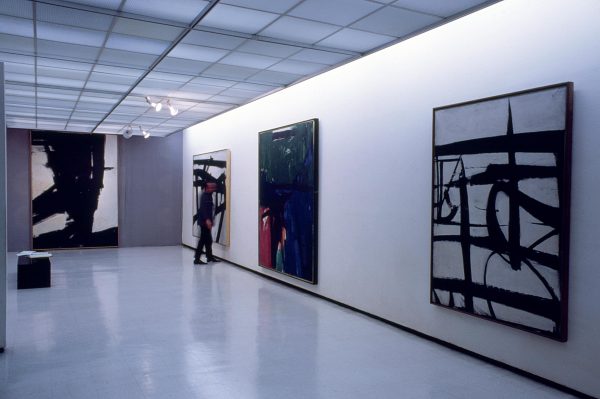 A visitor admires four large paintings hanging along a gallery wall.