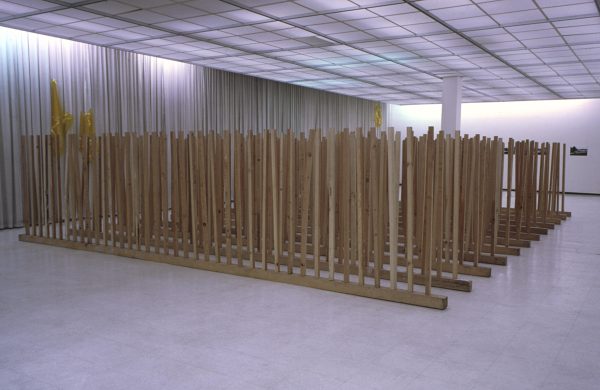 12 rows of many wooden posts inserted upright in 12 long wooden beams in an office like setting
