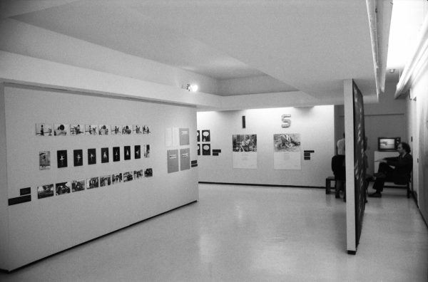 A gallery with several artworks on the wall and a person sitting behind a room divider.