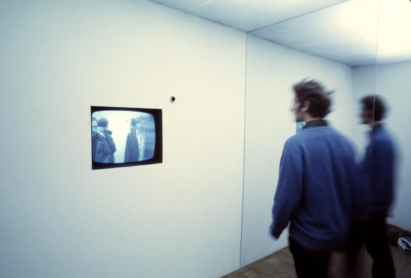 A person watching a video embedded in a wall in a mirrored room, doubling the whole scene