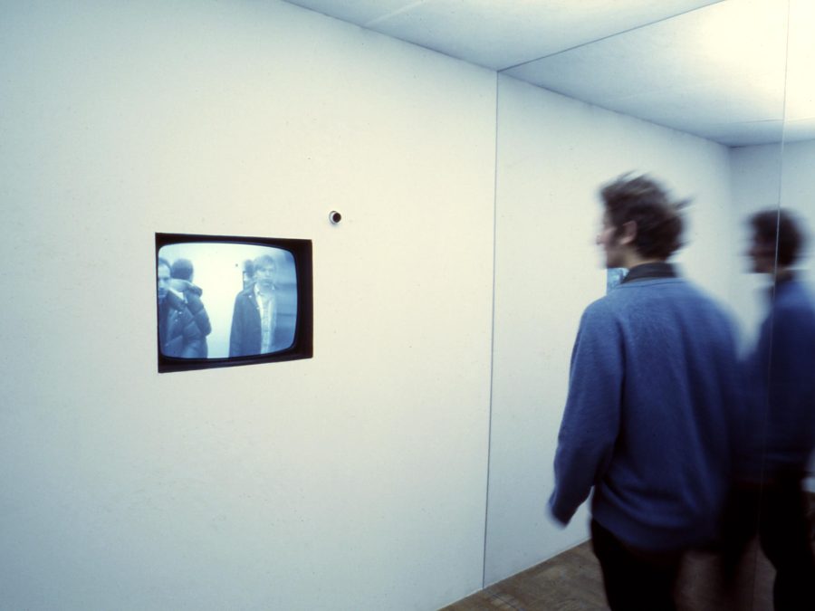A person watching a video embedded in a wall in a mirrored room, doubling the whole scene