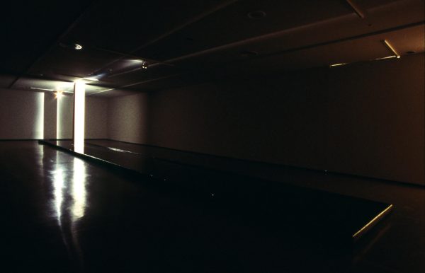 A spotlight highlights a white pillar in the back corner of an otherwise dark room