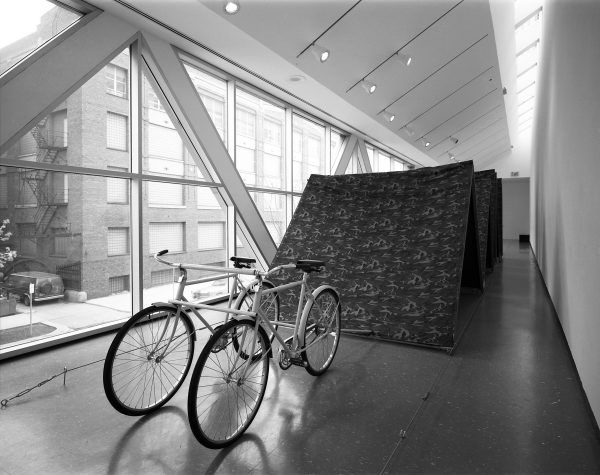 Two bikes attached to large fabric boards in a hallway with windows filling one side
